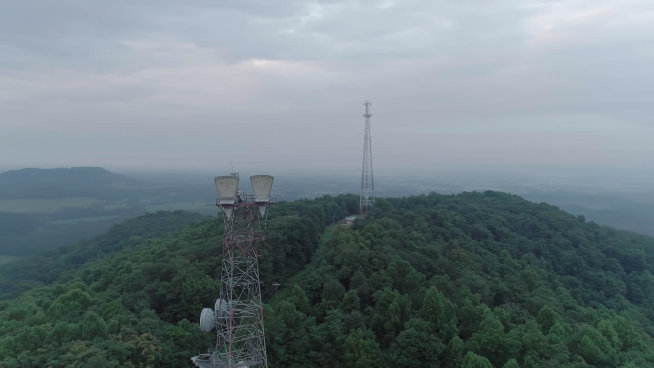 dron que rodea ampliamente dos torres de telecomunicaciones en la cima de una colina en una mañana nublada