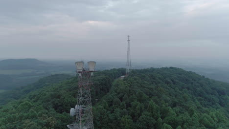 drone widely circling two telecommunication towers on top of hill on foggy morning