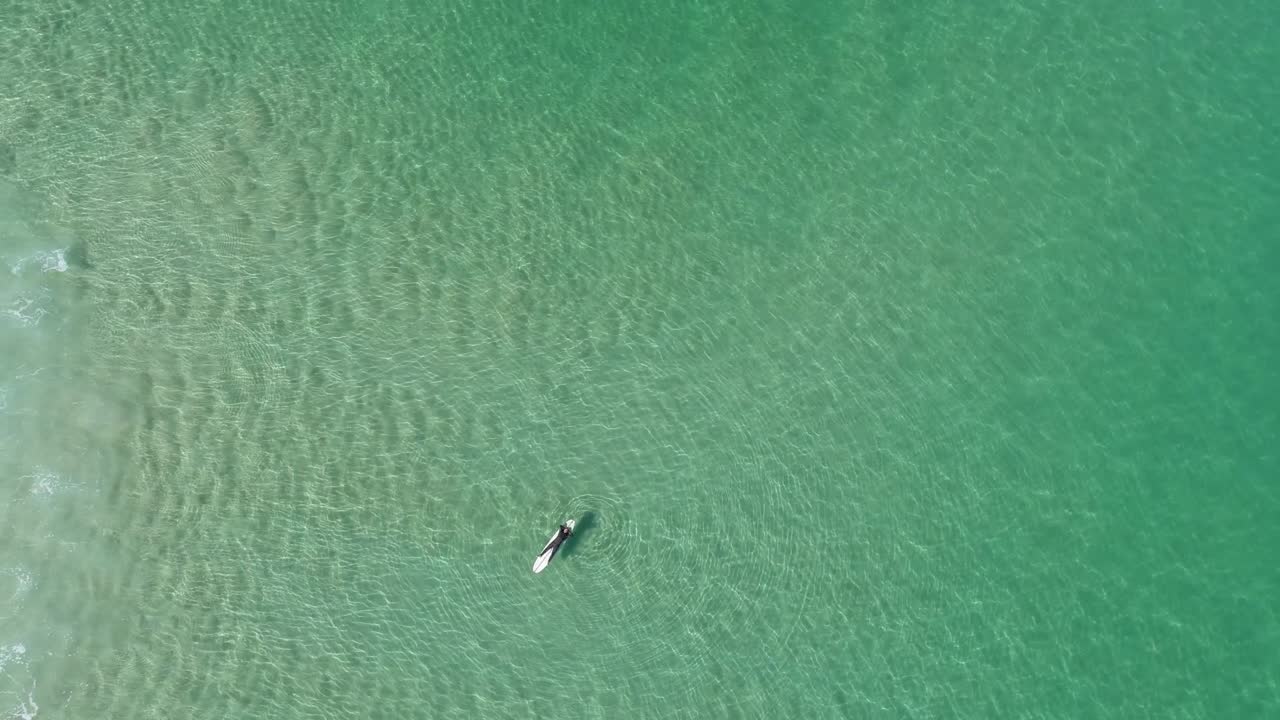 파도가 그 아래로 굴러갈 때 물 속에서 서핑 보드에 누워 쉬고 있는 한 남자의 공중 최고 전망