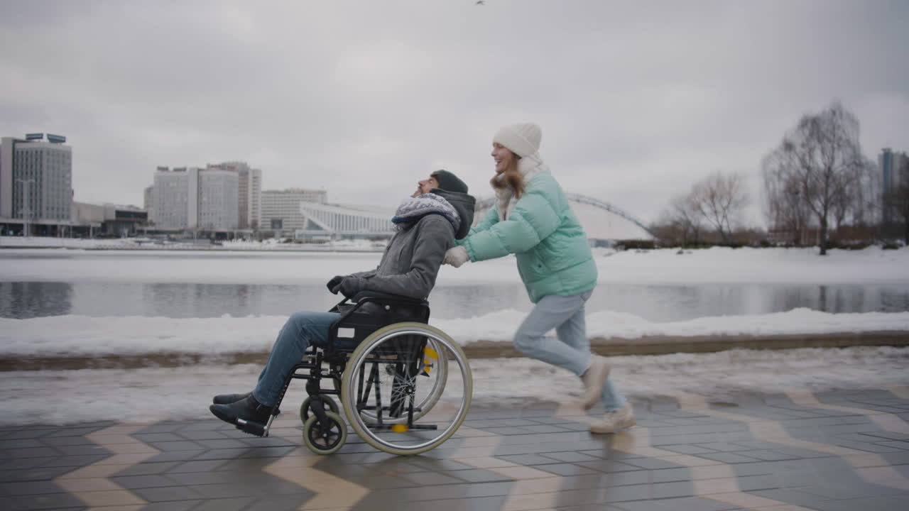 장애인 친구와 휠체어를 타고 달리며 겨울에 도시에서 함께 즐거운 시간을 보내는 행복한 여성