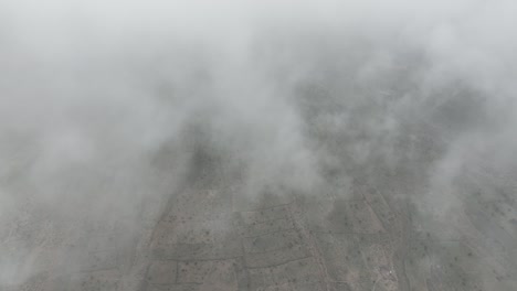 Aerial-drone-shot-flying-high-through-clouds-over-a-tiny-village-in-Tharparkar,-Sindh,-Pakistan-on-a-cloudy-day