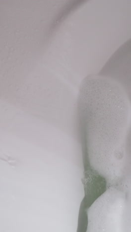 water and soap pouring down into foamy bathtub in washroom. filling basin with warm liquid to wash body and relax at home. comfortable hygiene