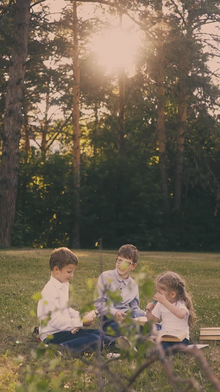 little girl helps brothers schoolboys do home assignments resting in green sunny garden in spring at back sunlight