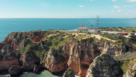 Ponta-da-Piedade-Lighthouse-over-limestone-headland-in-Lagos,-Algarve,-Portugal---Aerial-fly-in-wide-overview