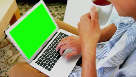 Man-using-laptop-while-having-coffee-in-living-room-at-home-4k