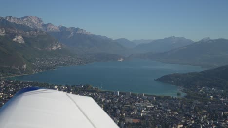 Lake-Annecy-in-the-French-Alps-with-village,-Aerial-airplane-side-shot