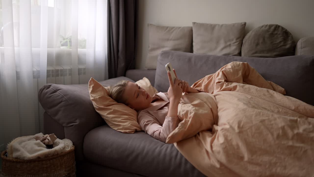여자 는 전화 를 들고 소파 에서 휴식 을 하고 있다