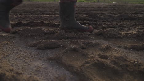 Granjero-Con-Botas-De-Goma-Caminando-Por-Un-Camino-Fangoso-Con-Huellas-De-Neumáticos,-De-Cerca