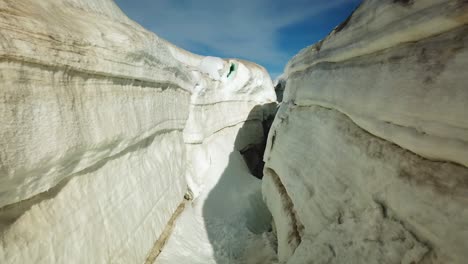 Aerial-view-inside-an-ice-crevasse,-cracked-on-the-ice-surface-of-an-icelandic-glacier,-on-a-sunny-day