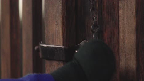 close-up of a hand pulling an old latch out of the lock of an old wooden gate