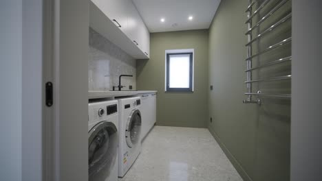 a functional laundry room equipped with modern appliances, a granite countertop, and a heated towel rail, set against a soothing olive-green wall and terrazzo flooring