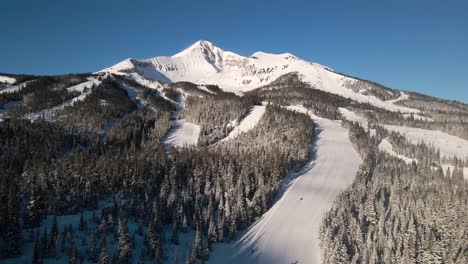 sweeping drone shot of big sky montana with a few skiers and snowboarders on the trail.