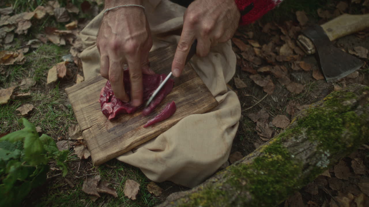 Hands of Man Slicing Raw Meat on Cutting Board Placed on Forest Ground