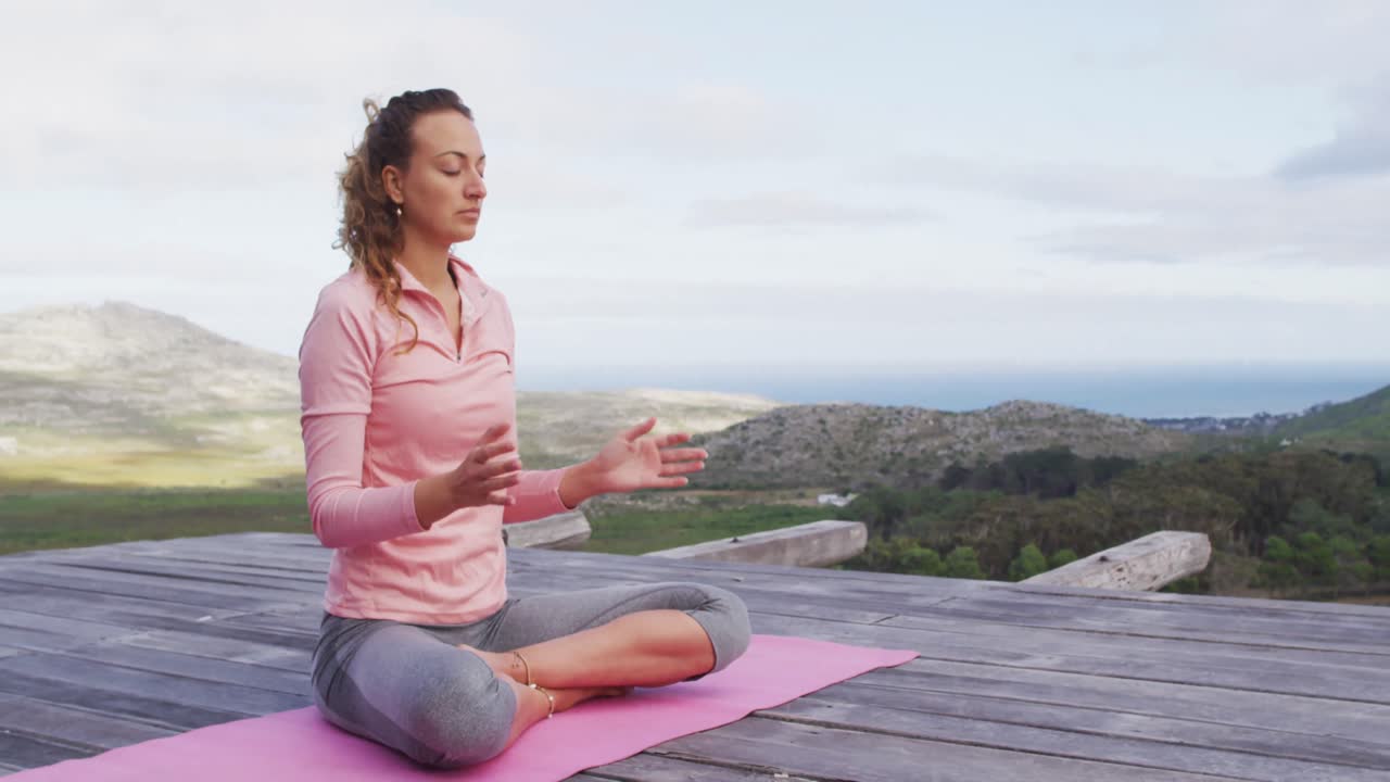 mujer caucásica practicando meditación de yoga sentada en la cubierta en la ladera de una montaña rural