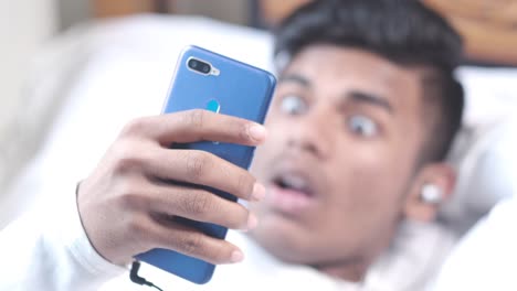 young man looking at smartphone in bed