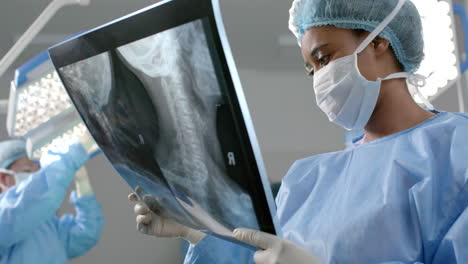 african american female surgeon looking at x-ray scans in operating theatre, slow motion