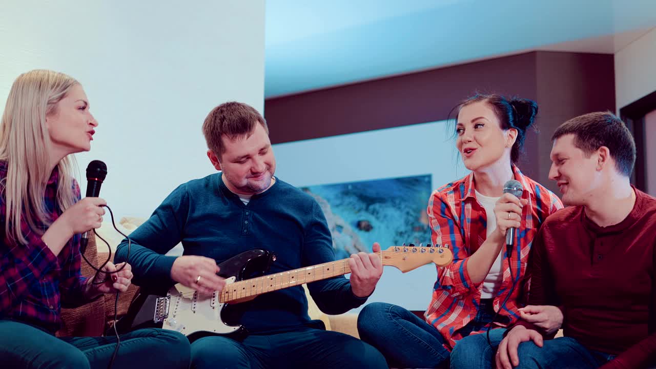 3명의 친구와 3명의 여자친구가 실내에서 노래를 부르고 기타를 연주합니다. 그들은 매우 행복하고 즐겁습니다.
