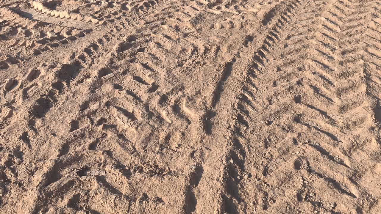 View of intricate tire patterns imprinted on soft earth. The golden-yellow soil creates a textured landscape of dusty trails left by passing vehicles