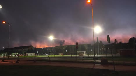people playing soccer or football at a stadium or a soccer field during night time or evening while sky has red and blue clouds and the stadium is being lit by stadium lights. running tracks visible.