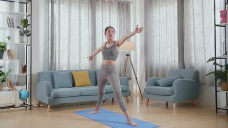 joven atleta asiática haciendo ejercicio, estirándose y practicando yoga en la postura del guerrero ii en casa. estilo de vida saludable, fitness, bienestar y concepto de atención plena