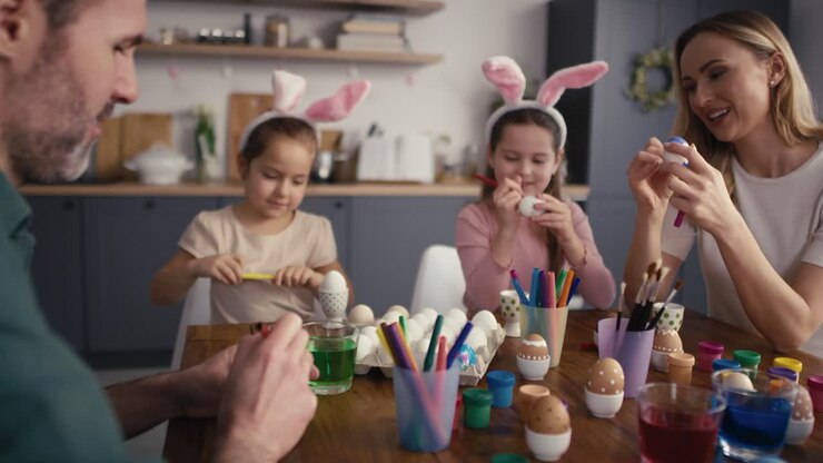 Zoom out of caucasian family of four people chatting and decorating easter eggs in domestic kitchen.