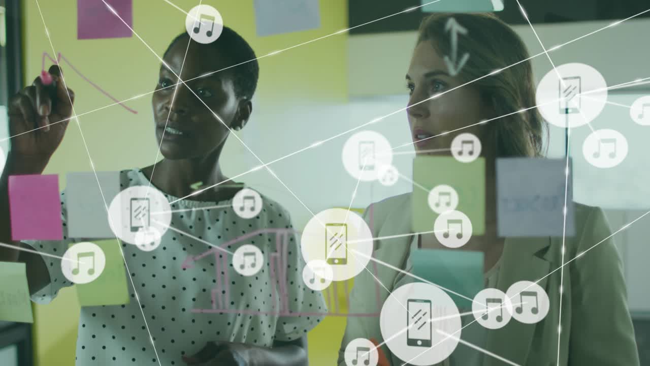 Two women business planning left writing pink pen on glass causing icons growing over sticky notes