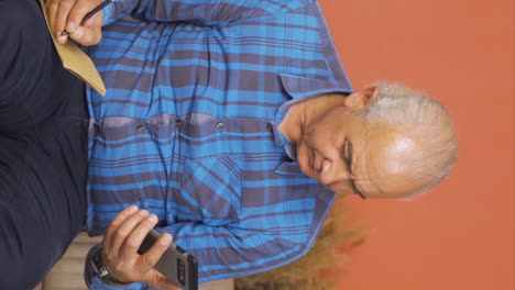 Vertical-video-of-Old-man-taking-notes-in-notebook.