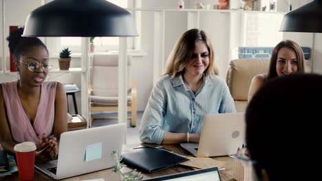 young happy beautiful multiethnic female colleagues discuss business by office table in stylish loft coworking space 4k