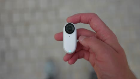 Overhead-View-Of-Insta360-Go-3-In-Palm-Of-Hand-With-Thumb-Pressing-Down-To-Turn-It-On