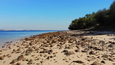 Drone-shot-flying-low-over-a-small-beach-with-rocks-and-stones-in-Troia,-Portugal