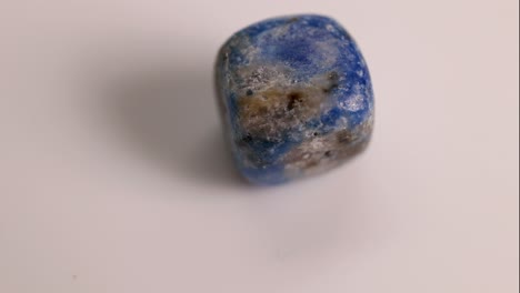 A Lapis Lazuli stone rotates on a white surface, highlighting its blue and gold hues under soft lighting