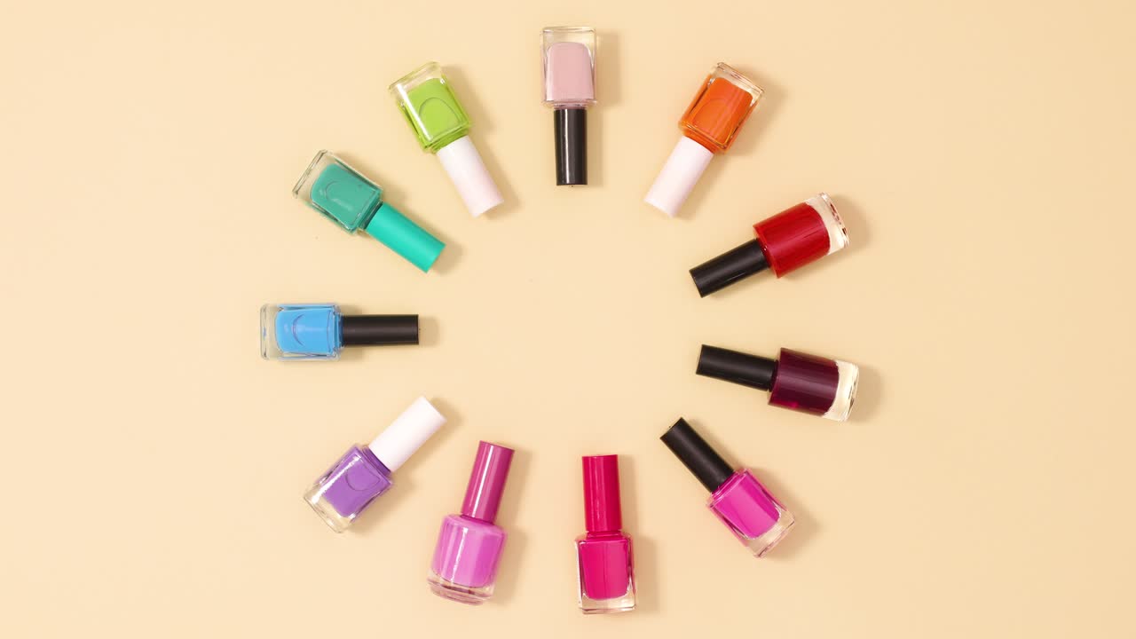 las botellas de esmalte de uñas de diferentes colores se mueven en círculo sobre un fondo beige. detenga el movimiento