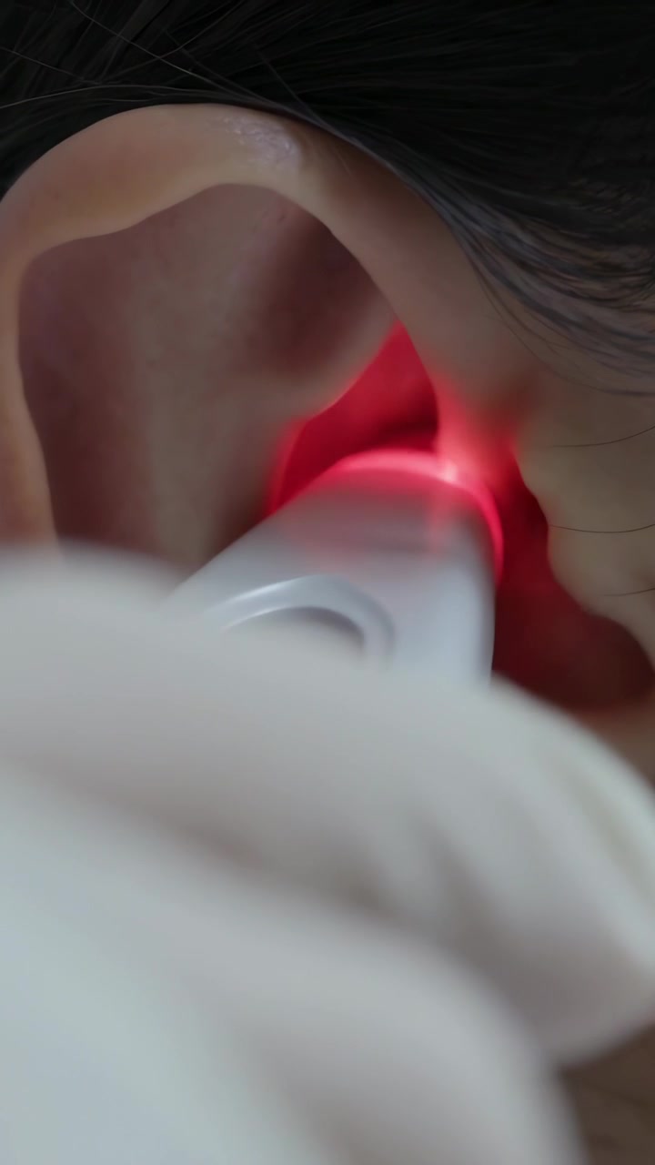Video verticale: Una mano guantata porta un dispositivo all'orecchio destro a casa per un rapido controllo, LED rosso.