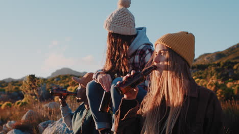 group of friends drinking together hanging out in beautiful countryside enjoying sunset on relaxed summer vacation