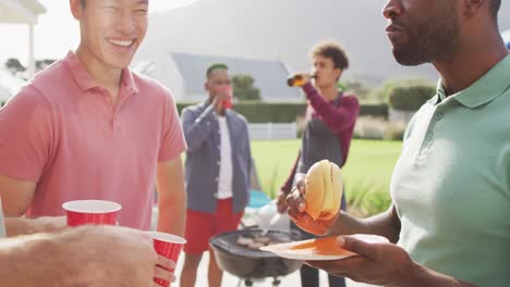 happy diverse male friends talking and drinking beer in garden on sunny day