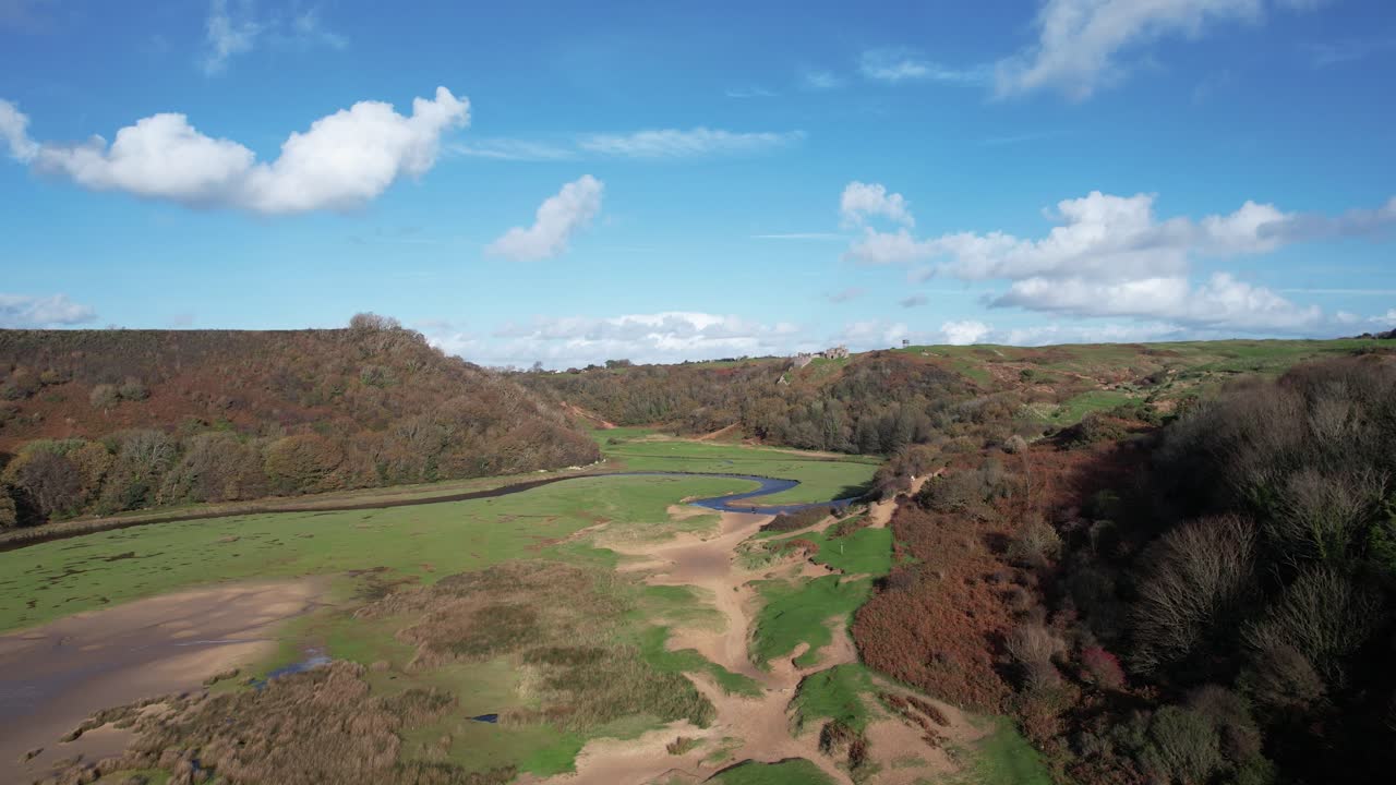 Forward flight from the sea into Three Cliffs Bay passing over Pennard Pill river and sandy shoreline in Wales
