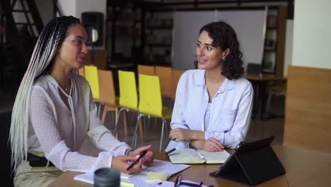 Dos-Mujeres-Con-Blusas-Blancas-Conversando-En-Una-Biblioteca-Abierta