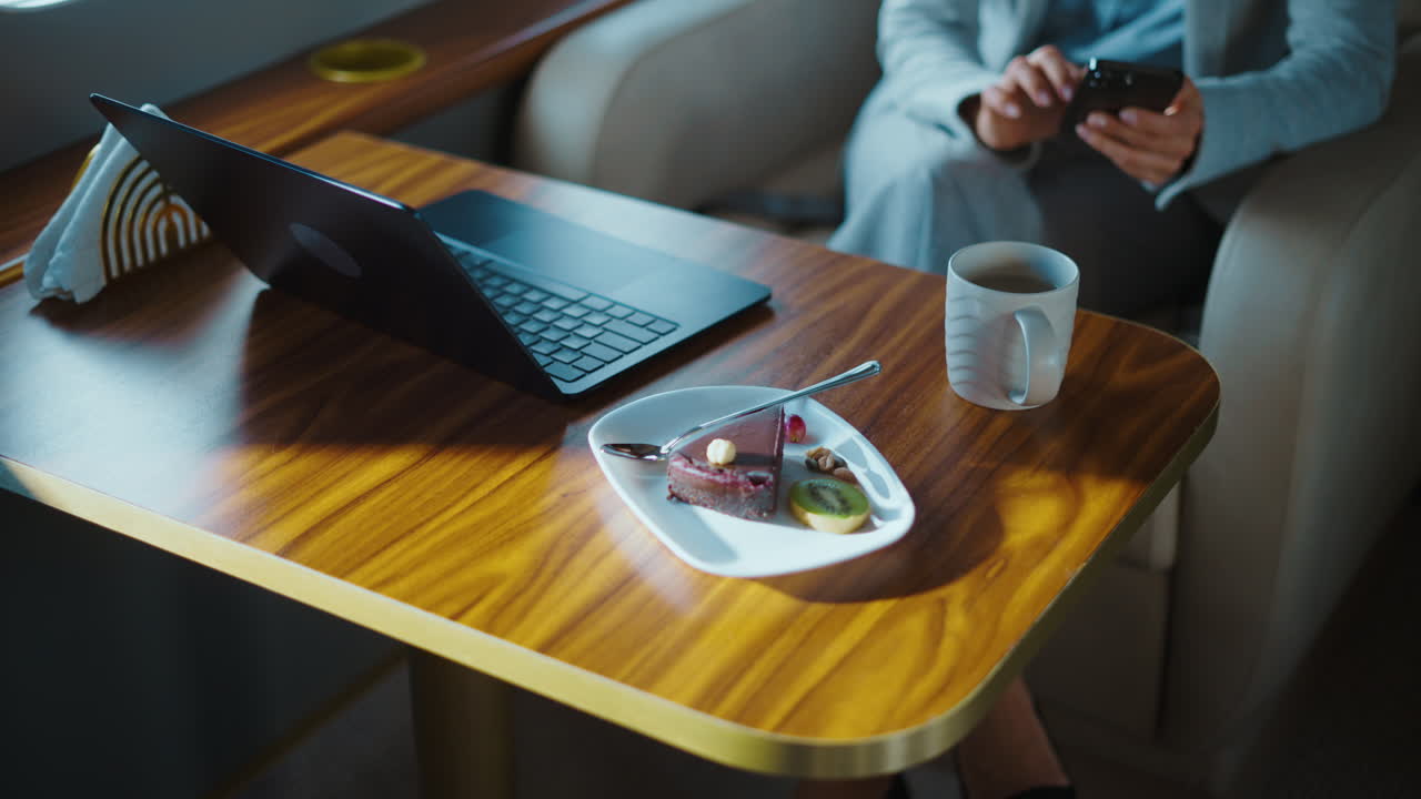 Businesswoman working on a private jet with laptop, dessert, and coffee