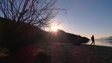 silhouette of people walking with dog at sunset on lake with mountains in background