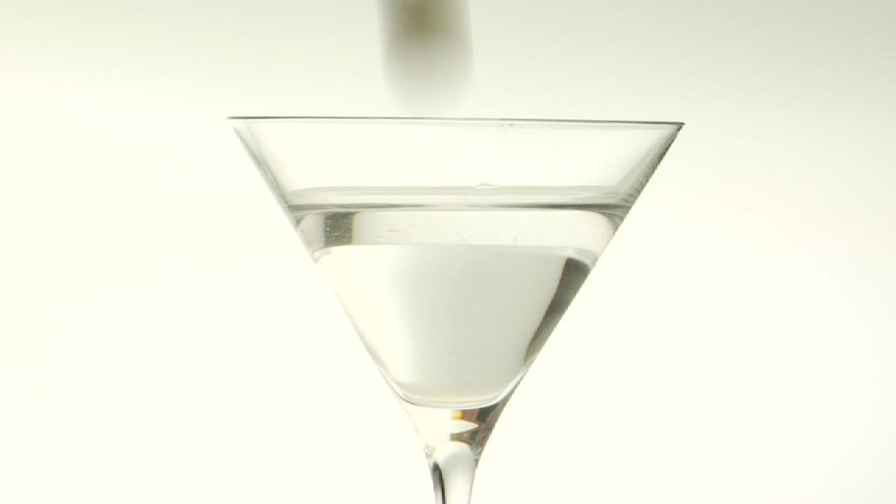 una aceituna verde se deja caer en un martini