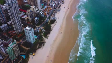 Aerial-tilting-top-down-view-of-a-beach-in-modern-skyscraper-city-on-a-cloudy-day