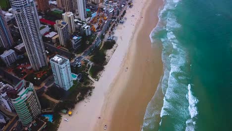 aerial tilting top down view of a beach in modern skyscraper city on a cloudy day