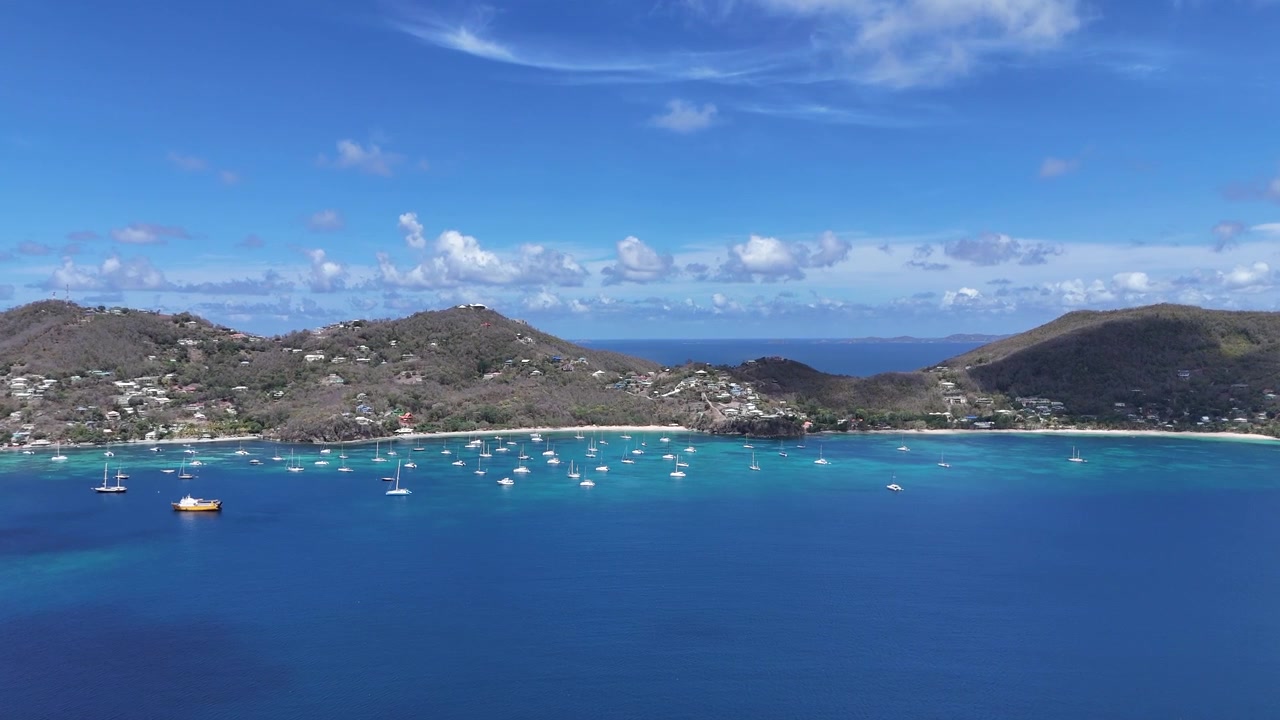 セントビンセントおよびグレナディーン諸島のベキア島にある深い青色の湾に、ヨットと帆船が停泊している広大なパノラマ空撮。