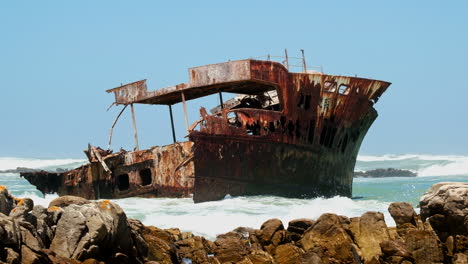 las olas chocan contra un viejo y oxidado naufragio en la costa de cabo agulhas.