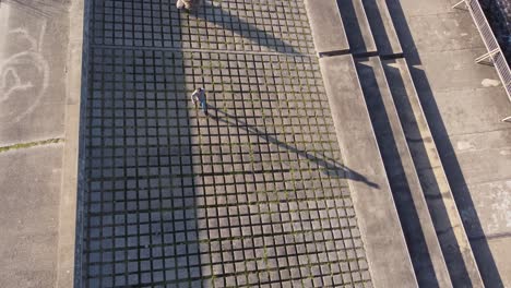 toma aérea de arriba hacia abajo de un hombre caminando sobre formas geométricas rocosas frente al océano a la luz del sol