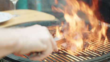 person using tongs to turn over juicy sirloin steak on flaming hot bbq grill with smoke rising from it