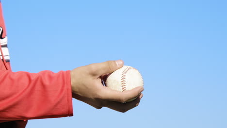 a hand tossing a baseball against a vibrant blue sky