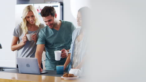 Friends-Looking-At-Laptop-And-Drinking-Coffee-In-Modern-Kitchen