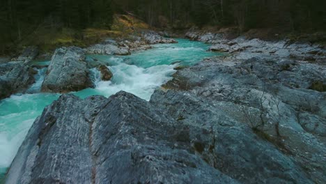 low aerial drone flight along a scenic and idyllic mountain river waterfall canyon with fresh blue water in the bavarian austrian alps, flowing down a beautiful riverbed along trees, forest and rocks