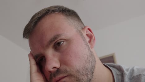 close up, an adult man sits alone against a wall, looking overwhelmed and weary, covering part of his face as he experiences inner tension and fatigue